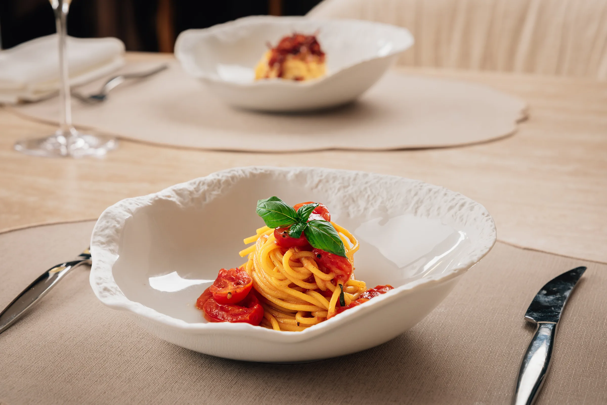 Spaghetti with datterino tomatoes and basil plated in a hand-finished bowl on a dressed private dining table